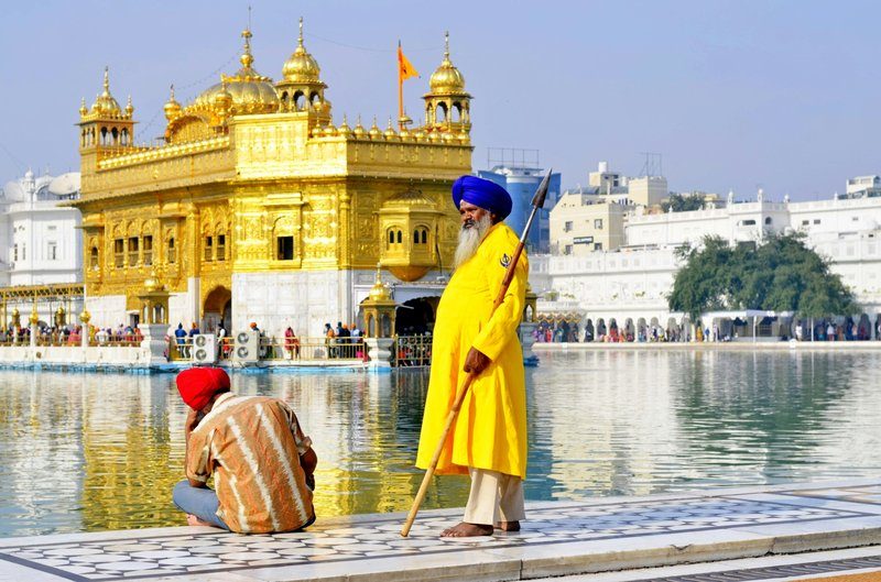Garde sikh en habit traditionnel devant le Temple d’Or à Amritsar, avec un pèlerin assis au bord du bassin sacré.