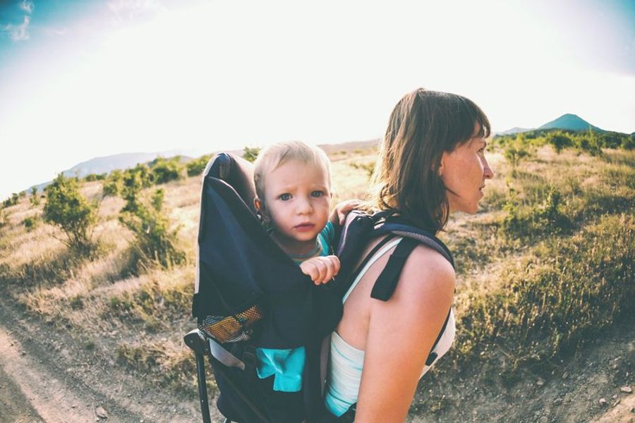 Maman portant son bébé en porte-bébé dorsal lors d’une randonnée sous le soleil