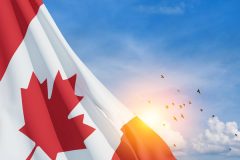 Drapeau du Canada flottant au vent avec un ciel bleu en arrière-plan, accompagné d'un coucher de soleil et d'un groupe d'oiseaux en vol