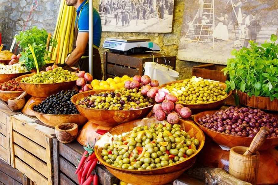 Étals colorés de produits locaux au marché provençal, avec des olives, légumes et herbes.