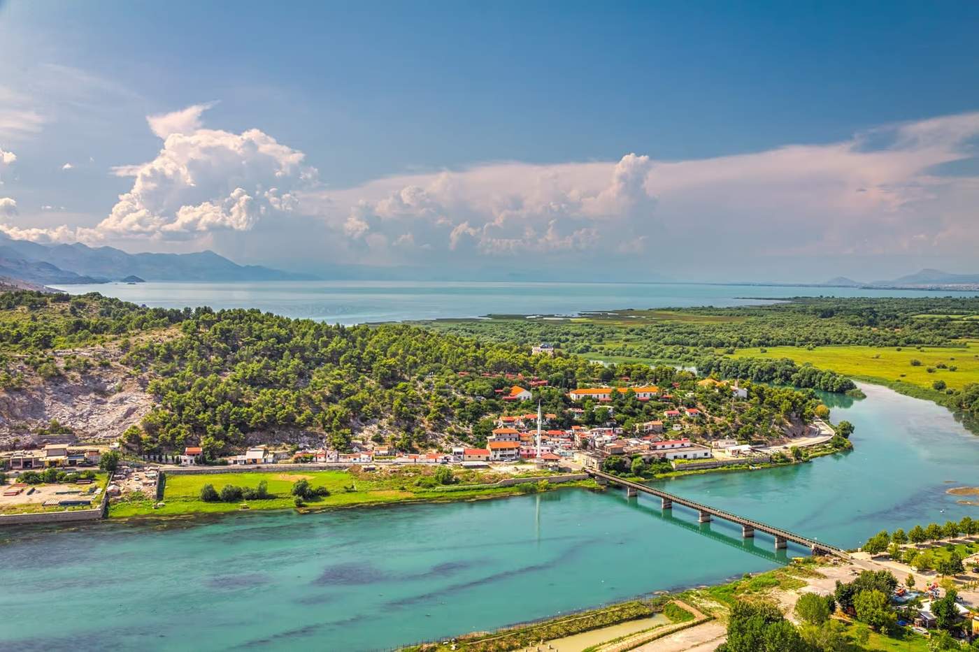 Vue panoramique sur la ville de Shkodër avec la rivière, les collines et le lac Skadar en arrière-plan sous un ciel dégagé.