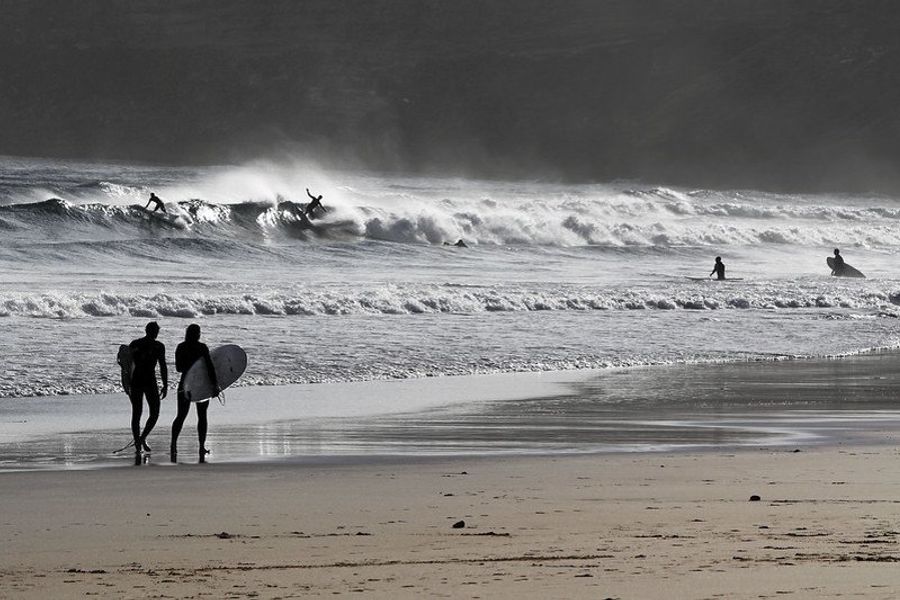 Surfeurs sur la plage de Sagres avec des vagues impressionnantes en arrière-plan.