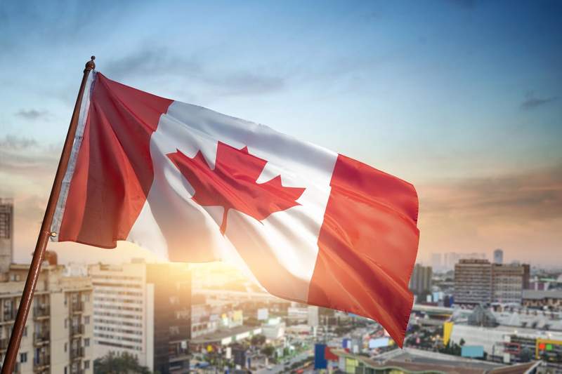 Drapeau du Canada flottant au-dessus d’une ville au coucher du soleil