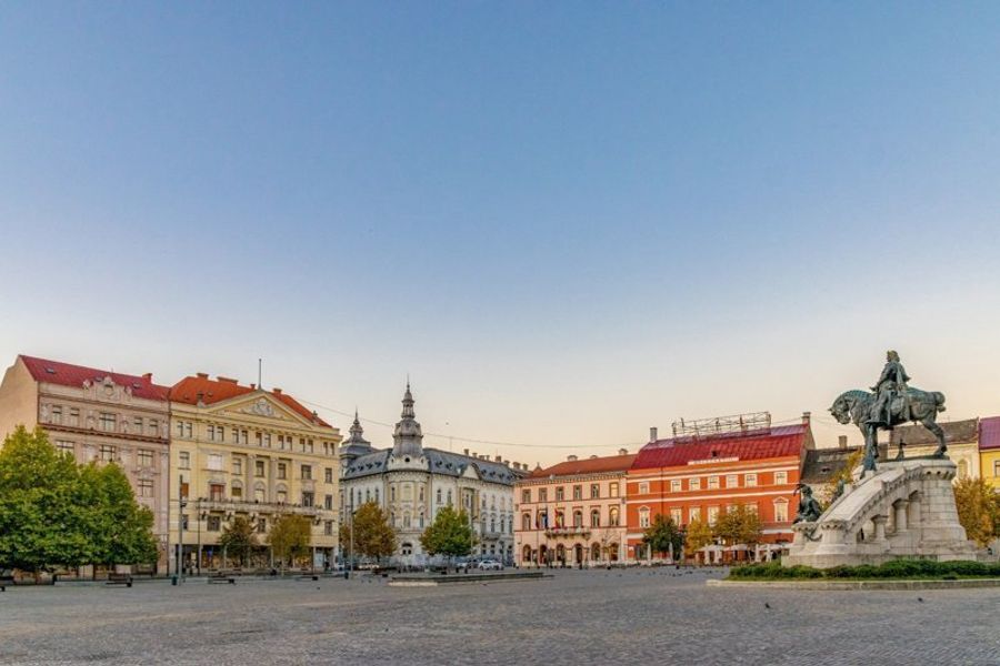 Place Unirii à Cluj-Napoca avec des bâtiments historiques et la statue de Matthias Corvin.