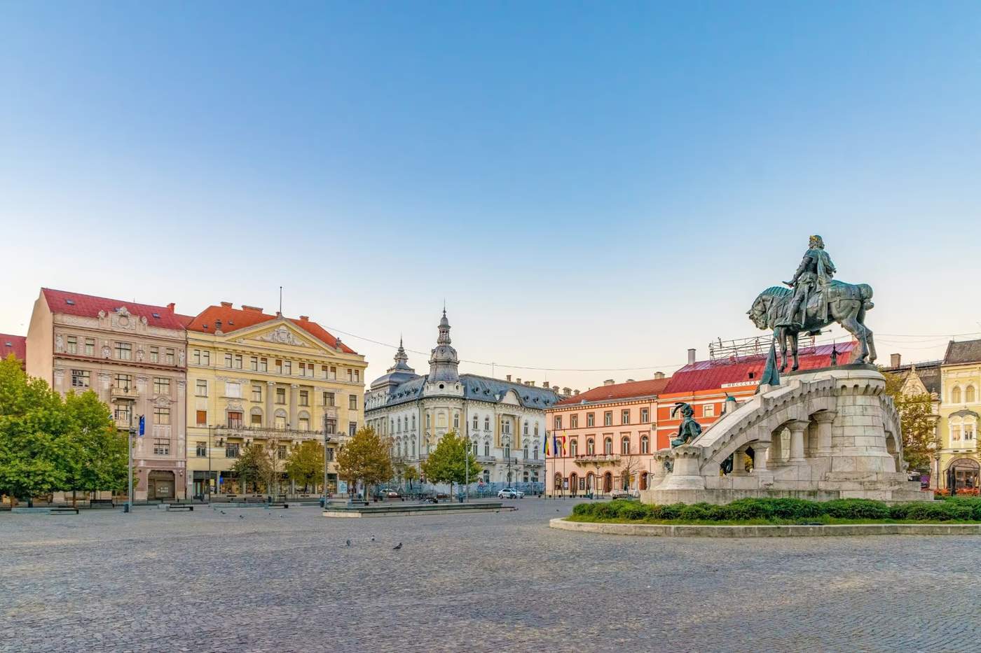 Place Unirii à Cluj-Napoca avec des bâtiments historiques et la statue équestre de Matthias Corvin au centre de la place.
