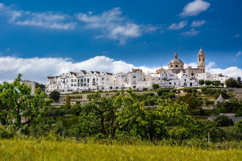 Vue panoramique de Locorotondo, un village blanc typique des Pouilles, entouré de champs verts.