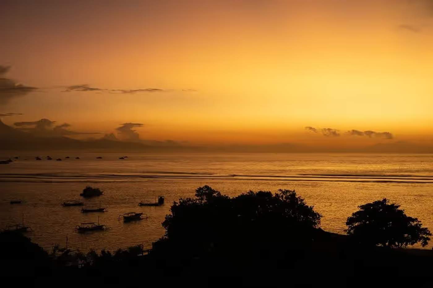 Lever du soleil à Sanur avec des silhouettes de bateaux traditionnels balinais sur l'eau calme.