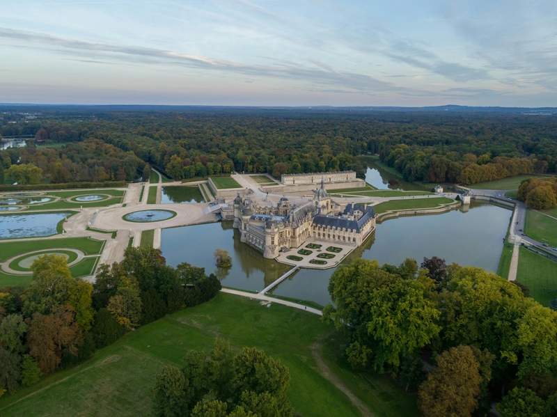 Vue aérienne du château de Chantilly et de ses jardins à la française entourés d’eau dans l’Oise.