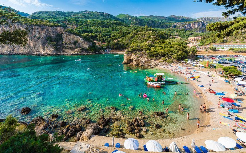 Plage de Paleokastritsa avec des eaux cristallines, entourée de collines verdoyantes et de baigneurs.