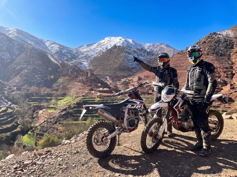 Deux pilotes et leurs motos enduro dans la vallée de l’Ourika, face aux montagnes de l’Atlas marocain