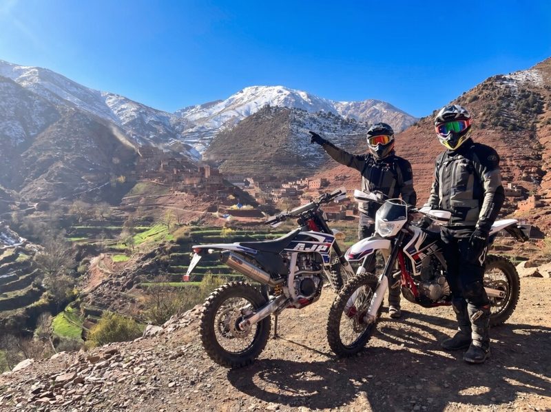 Deux pilotes et leurs motos enduro dans la vallée de l’Ourika, face aux montagnes de l’Atlas marocain