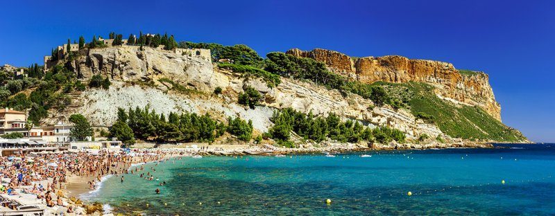 Plage animée de Cassis avec le Cap Canaille en arrière-plan.