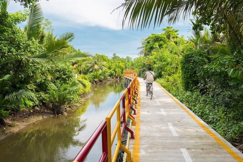 Un homme à vélo sur une piste traversant une zone verte à Bang Krachao.
