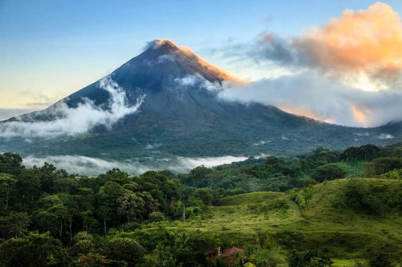Vue du volcan Arenal au Costa Rica avec des nuages couvrant partiellement le sommet et une végétation luxuriante au premier plan. 
