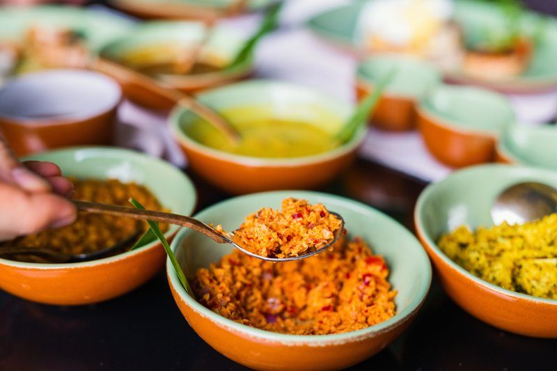 Gros plan sur une cuillère de sambol, un condiment épicé sri-lankais à base de noix de coco râpée, servie avec divers currys dans des bols en céramique.