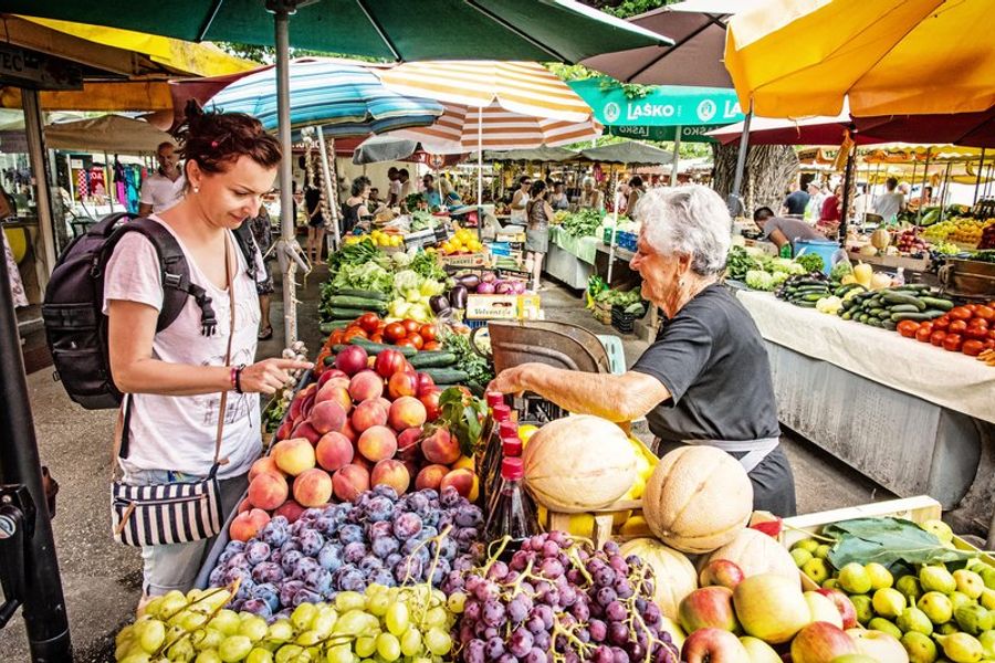 Scène animée du marché de Trogir avec des étals de fruits et légumes colorés.