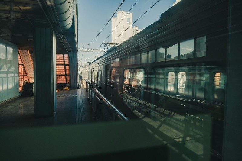 Train entrant en gare en Corée du Sud, vu depuis le quai avec reflets sur les vitres et bâtiments urbains en arrière-plan.