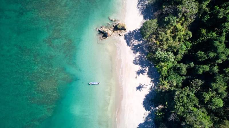 Vue aérienne d'une plage immaculée de l'Isla Tortuga, avec une mer turquoise et un petit bateau amarré au bord de la plage, entourée d'une végétation luxuriante.