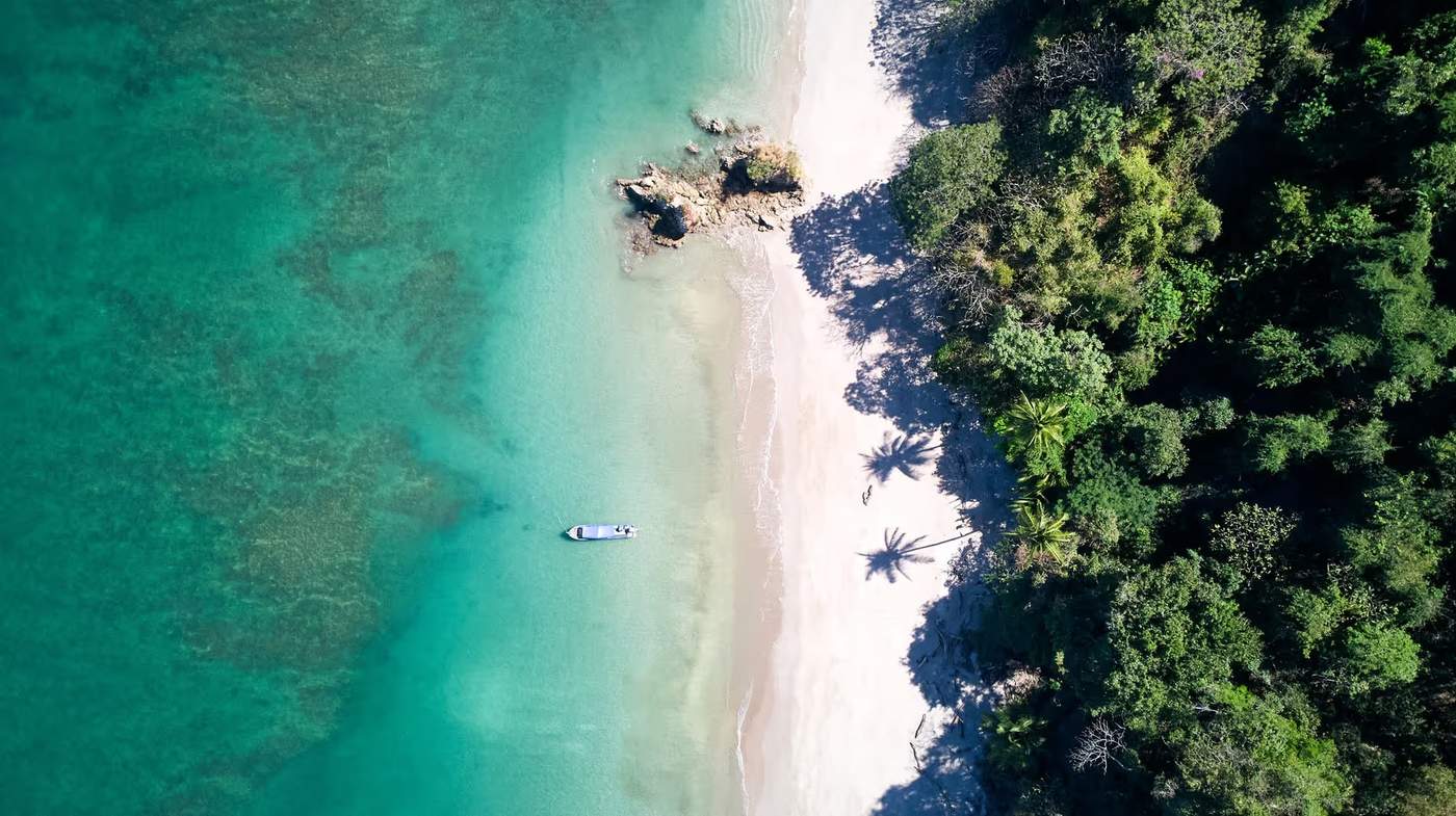 Vue aérienne d'une plage immaculée de l'Isla Tortuga, avec une mer turquoise et un petit bateau amarré au bord de la plage, entourée d'une végétation luxuriante.