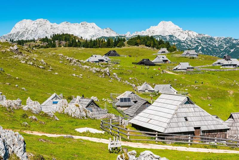 Vue des chalets traditionnels de Velika Planina en Slovénie avec les Alpes slovènes en arrière-plan.
