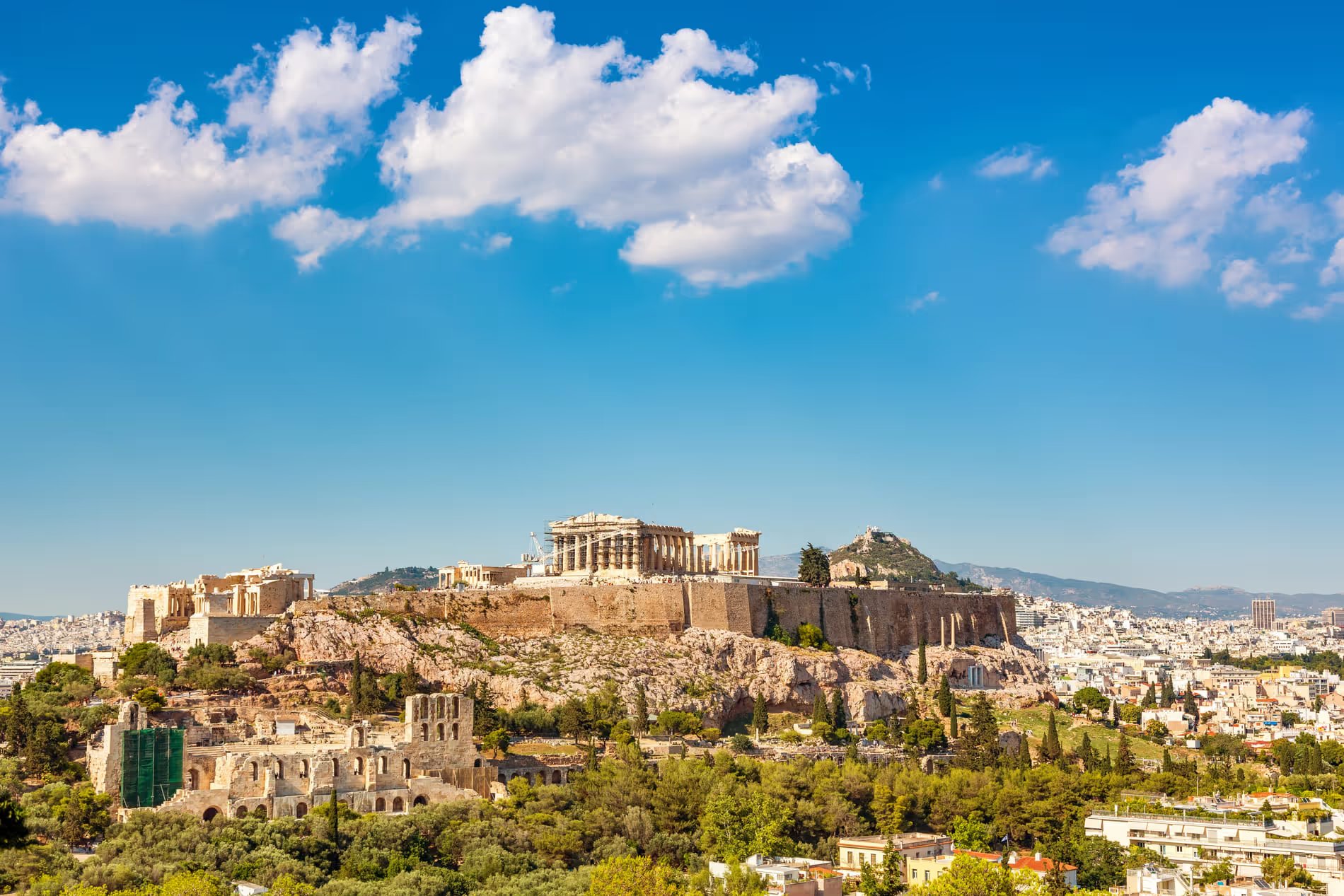 Vue panoramique de l'Acropole d'Athènes, avec le Parthénon dominant la colline, sous un ciel bleu clair.