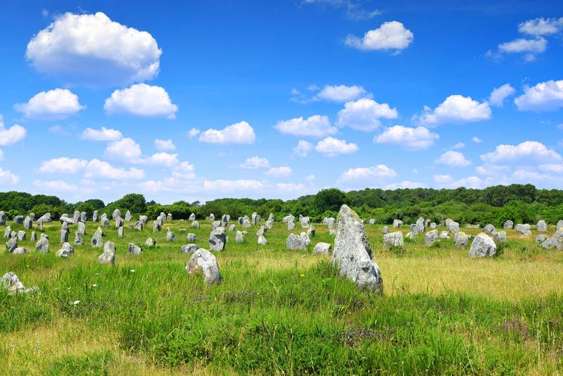 Vue panoramique des alignements de menhirs à Carnac, en Bretagne, sous un ciel bleu parsemé de nuages.