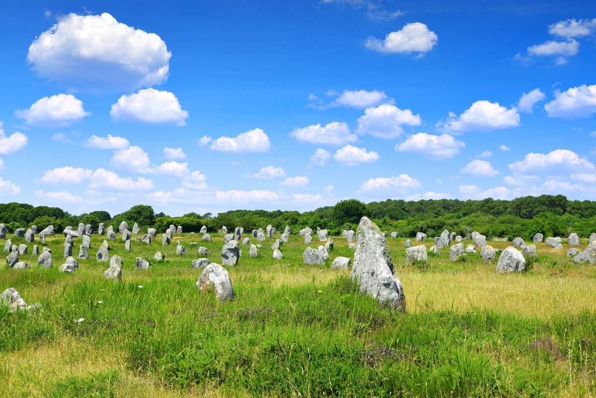 Vue panoramique des alignements de menhirs à Carnac, en Bretagne, sous un ciel bleu parsemé de nuages.