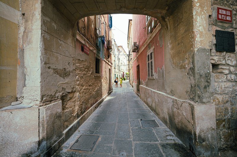 Ruelle pavée du centre historique de Piran avec arche en pierre et façades colorées, Slovénie