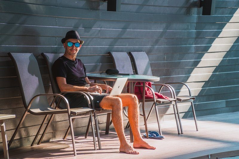 Homme assis au bord de la piscine, travaillant sur son ordinateur portable dans une ambiance détendue en plein air.