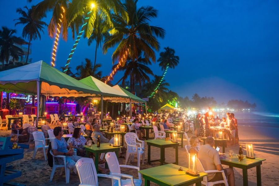 Ambiance nocturne sur la plage de Mirissa avec des restaurants en plein air, des tables éclairées par des lanternes et des palmiers décorés de lumières colorées.