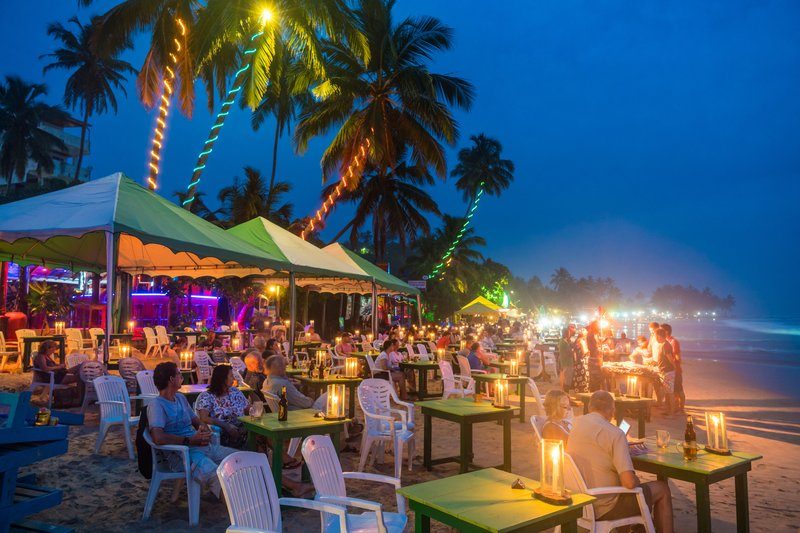Ambiance nocturne sur la plage de Mirissa avec des restaurants en plein air, des tables éclairées par des lanternes et des palmiers décorés de lumières colorées.