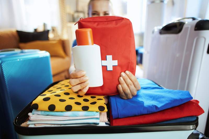 Trousse de premiers secours rouge et bouteille de lotion tenues au-dessus d’une valise en cours de préparation.