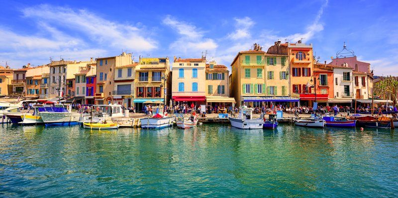 Vue sur le port de Cassis avec ses façades colorées, ses bateaux amarrés et une ambiance animée en bord de mer.