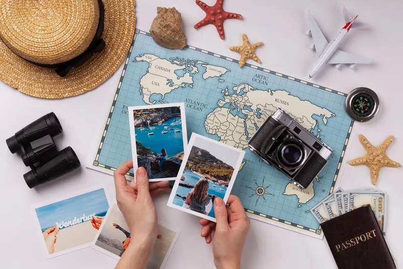 Flatlay de voyage avec carte du monde, photos imprimées, appareil photo vintage, passeport, billets, jouets en forme d’étoiles de mer, chapeau et jumelles.