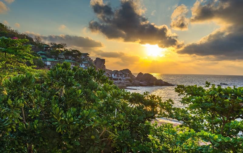 Magnifique coucher de soleil sur Koh Tao, avec des maisons en bord de mer entourées de verdure luxuriante.