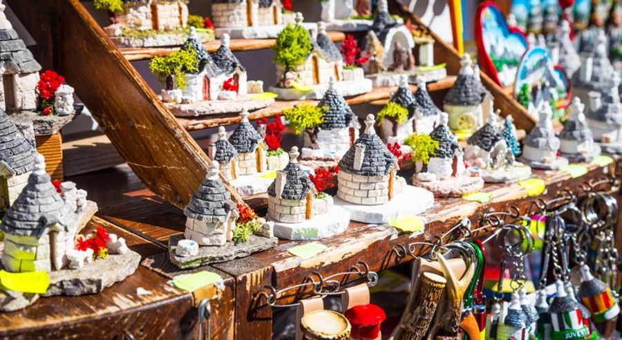 Stands colorés vendant des souvenirs artisanaux représentant des trulli, dans un marché local ensoleillé.