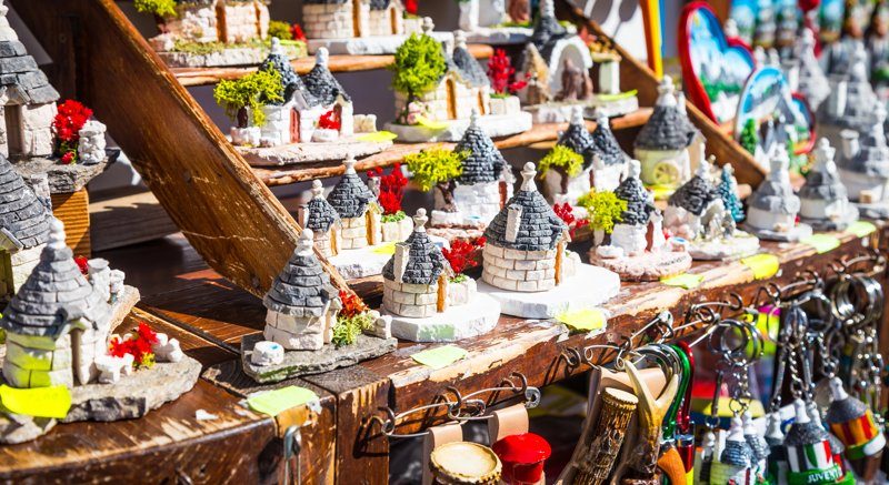 Stands colorés vendant des souvenirs artisanaux représentant des trulli, dans un marché local ensoleillé.