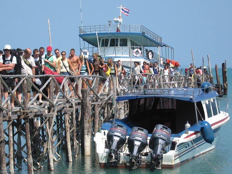 Des touristes se tenant sur un ponton en bois avec un bateau à moteur amarré, prêt à partir.