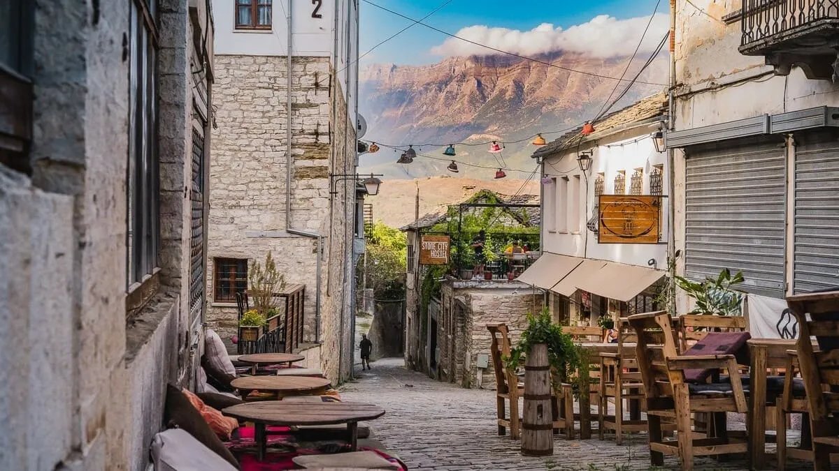 Ruelle pavée de Gjirokastër bordée de maisons traditionnelles et de terrasses, avec vue sur les montagnes albanaises