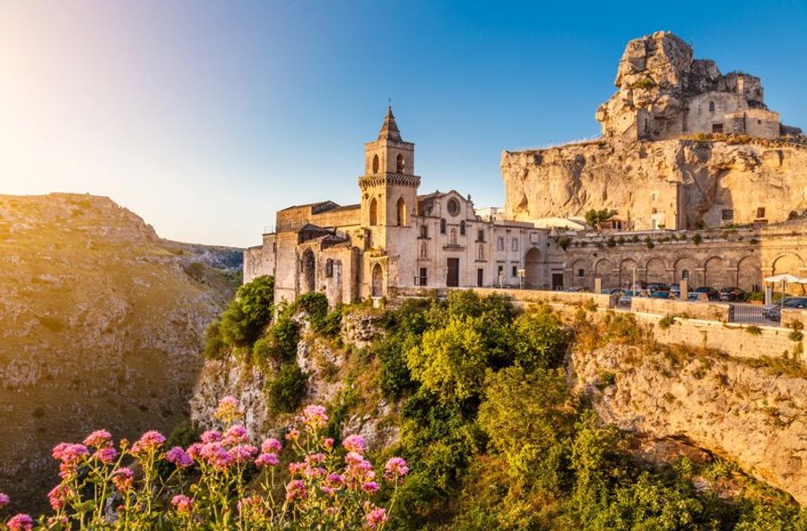 Vue pittoresque de la cathédrale de Matera, en Italie, au coucher du soleil, surplombant un paysage de falaises et de fleurs en premier plan.