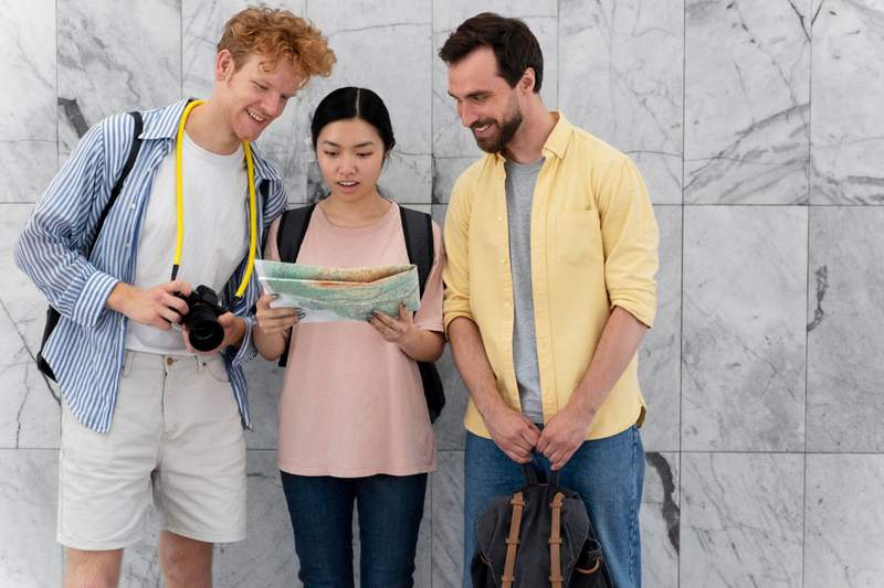 Trois voyageurs consultant une carte routière pour organiser leur road trip, avec appareil photo et sac à dos