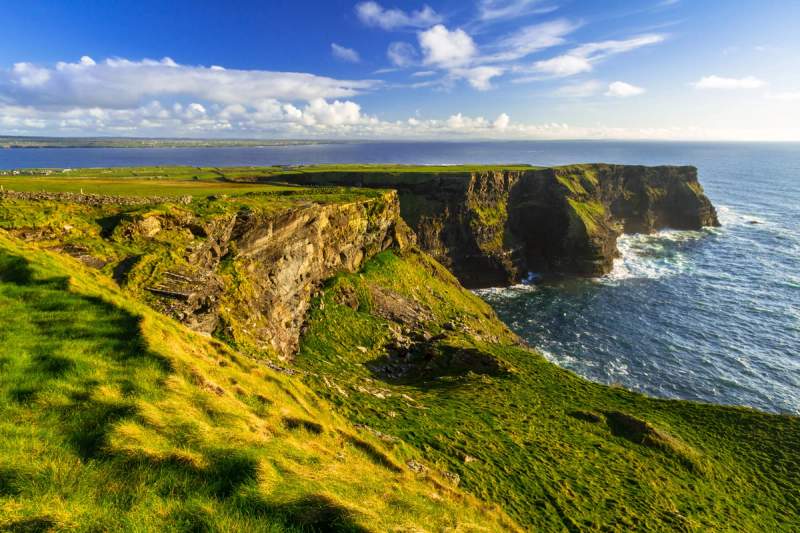 Vue des falaises d'Irlande, s'élevant majestueusement au-dessus de l'océan Atlantique, sous un ciel bleu et ensoleillé.