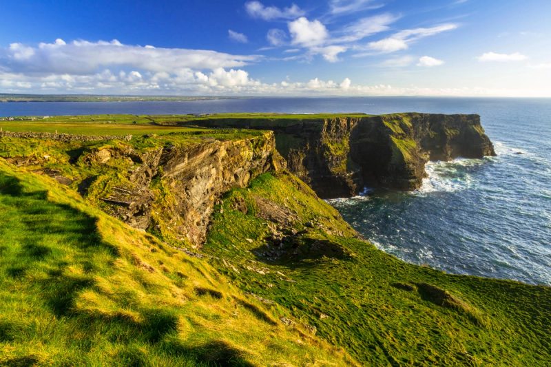Vue des falaises d'Irlande, s'élevant majestueusement au-dessus de l'océan Atlantique, sous un ciel bleu et ensoleillé.