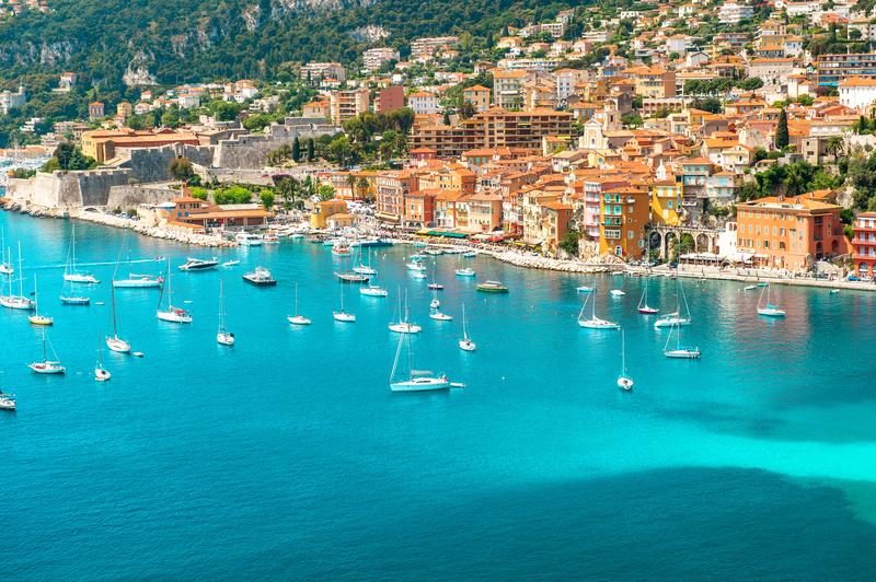 Vue panoramique de Nice avec ses maisons colorées et ses voiliers sur la Méditerranée.