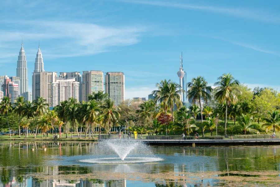 Parc Titiwangsa avec un lac, des fontaines et des palmiers, offrant une vue sur la skyline de Kuala Lumpur.