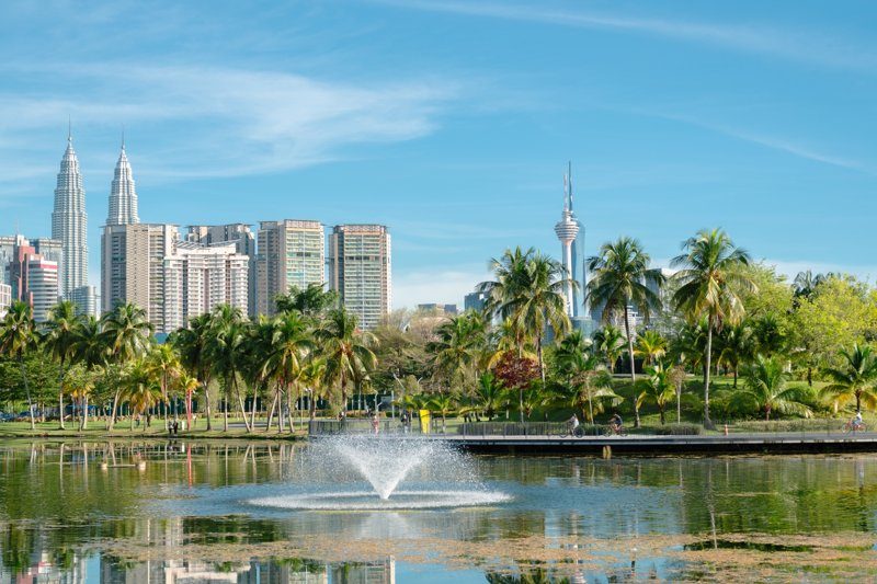 Parc Titiwangsa avec un lac, des fontaines et des palmiers, offrant une vue sur la skyline de Kuala Lumpur.