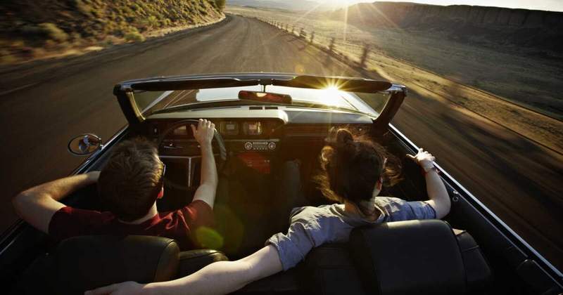 Deux voyageurs roulent dans une décapotable au coucher du soleil sur une route déserte, symbole de liberté et d’aventure en road trip.