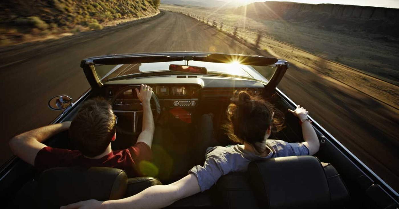 Deux voyageurs roulent dans une décapotable au coucher du soleil sur une route déserte, symbole de liberté et d’aventure en road trip.