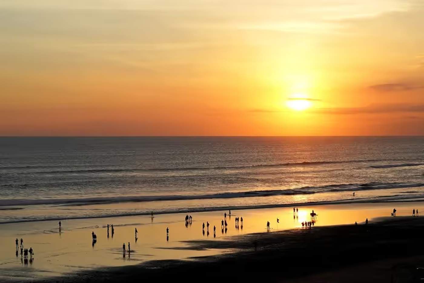 Coucher de soleil sur la plage de Seminyak avec des silhouettes au bord de l'eau, Bali.