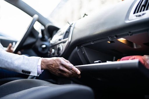 Main d'un conducteur ouvrant la boîte à gants de sa voiture sur le tableau de bord.